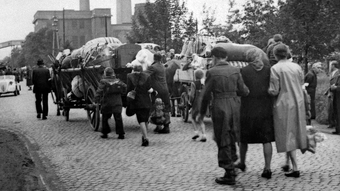 Flüchtlinge gehen mit beladenen Wagen und Gepäck über eine gepflasterte Straße.