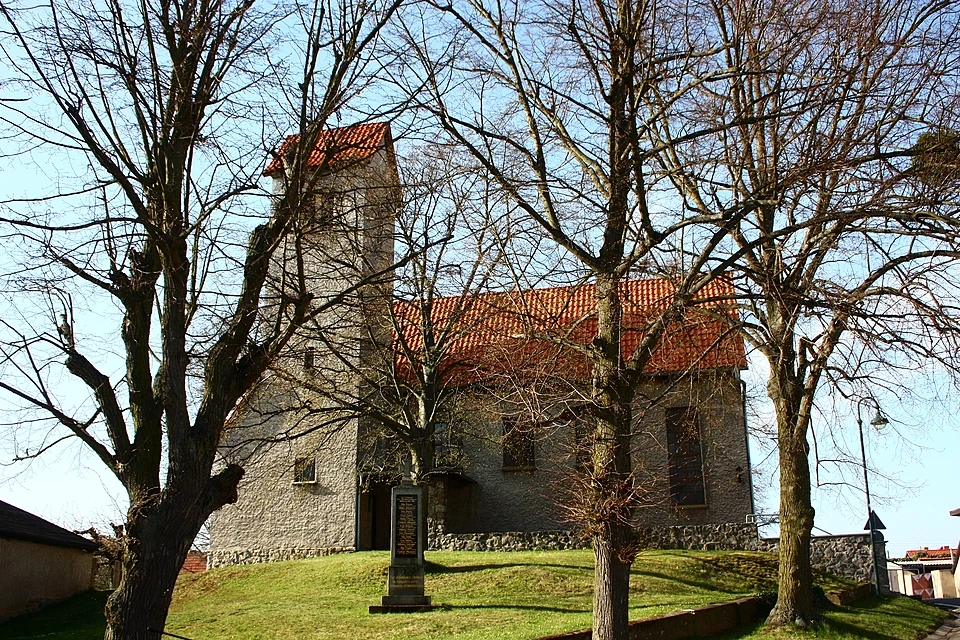 St. Wilhelm in Tilkerode mit hellem Putz, rotem Ziegeldach, Turm und alten Bäumen