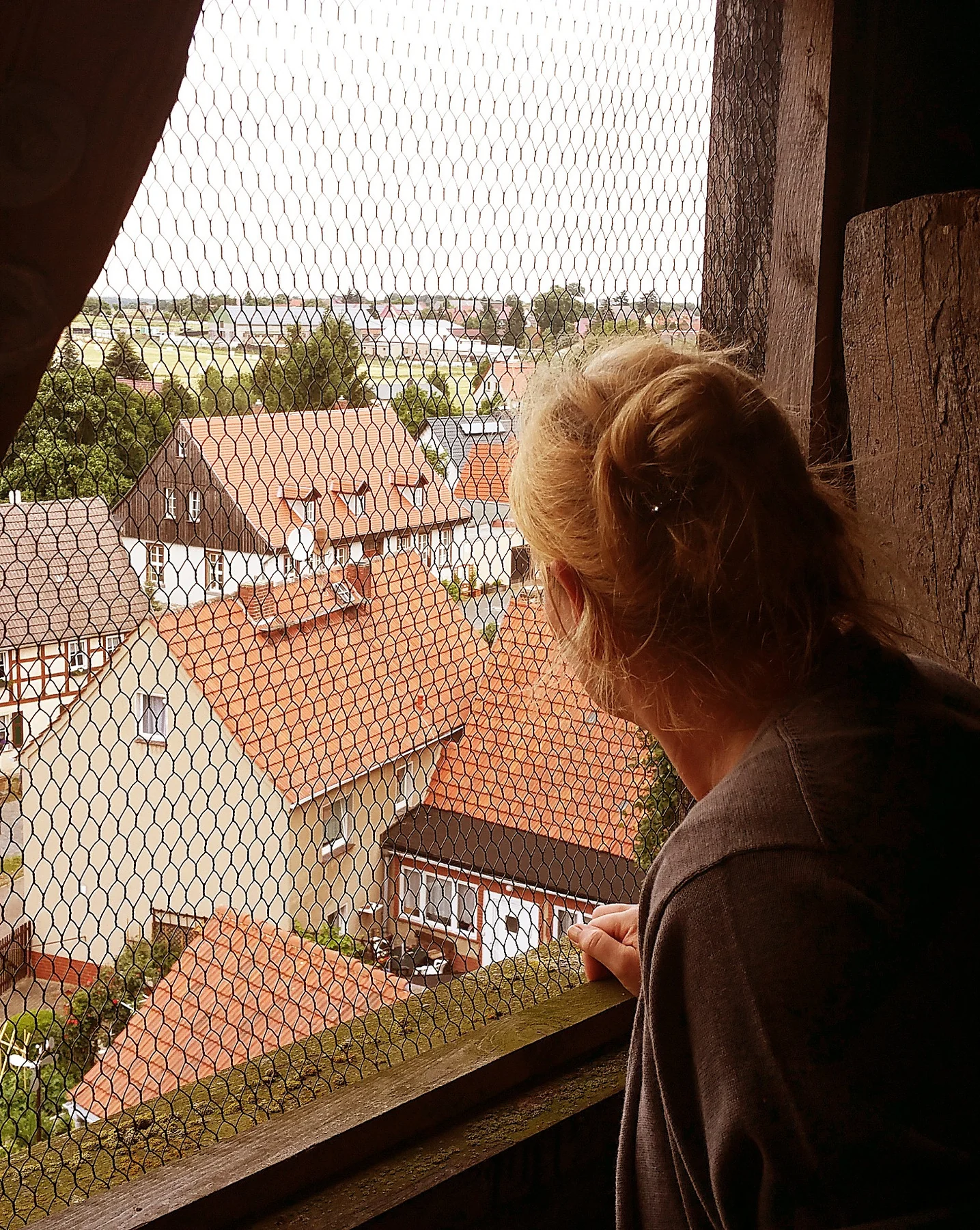 Besucherin blickt durch das Schutzgitter einer Turmöffnung auf Fachwerkhäuser und rote Dächer in Abberode