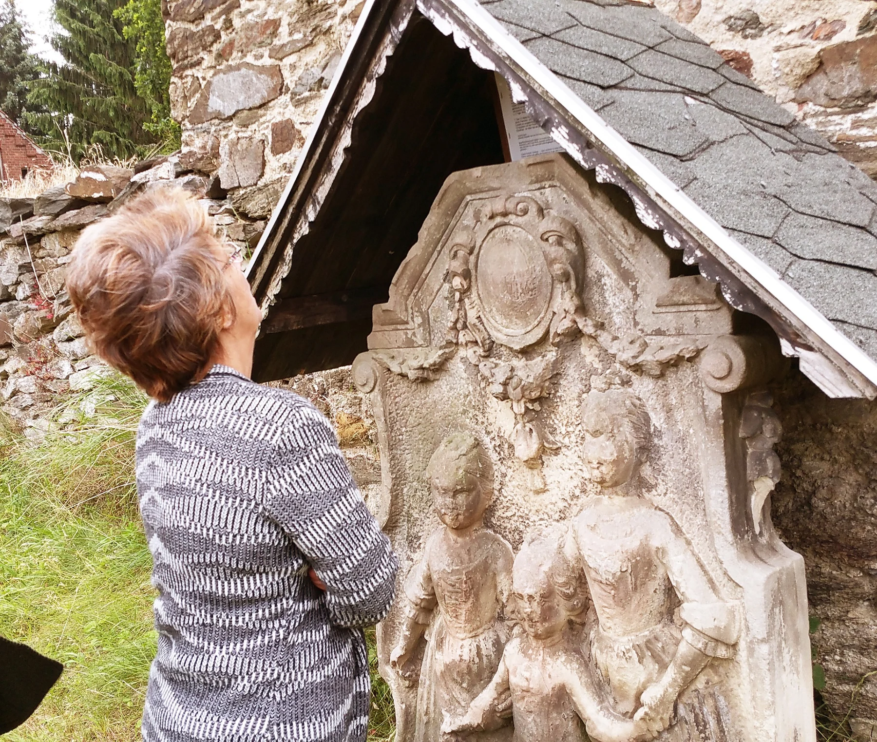 Besucherin vor einem verzierten Steinrelief unter einem kleinen Schutzdach am Abberöder Kirchturm