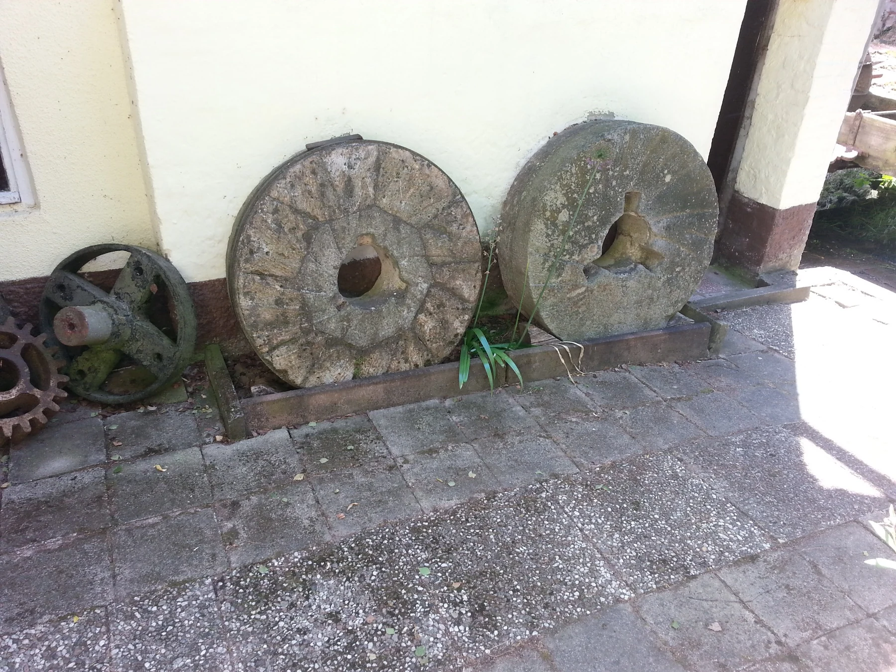 Zwei alte Mühlsteine sowie Metallräder an der Außenwand der Untermühle