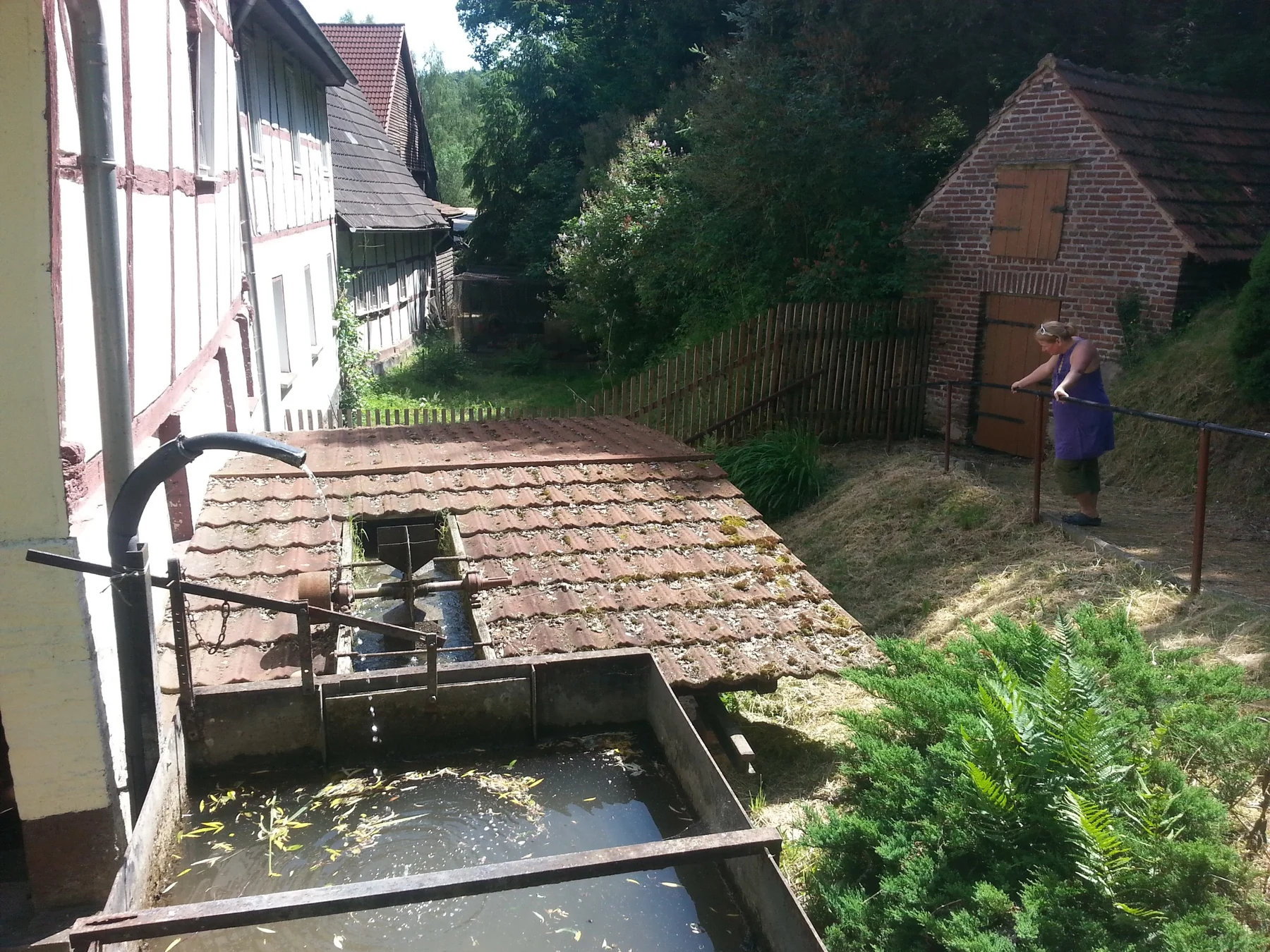 Wasserbecken und gedeckter Bereich am Fachwerkgebäude der Untermühle mit Besucherin am Geländer